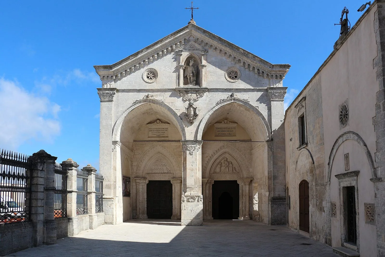 La facciata in pietra chiara del santuario di San Michele Arcangelo a Monte Sant'Angelo, con i due grandi archi d'ingresso e la statua dell'Arcangelo sopra il portale