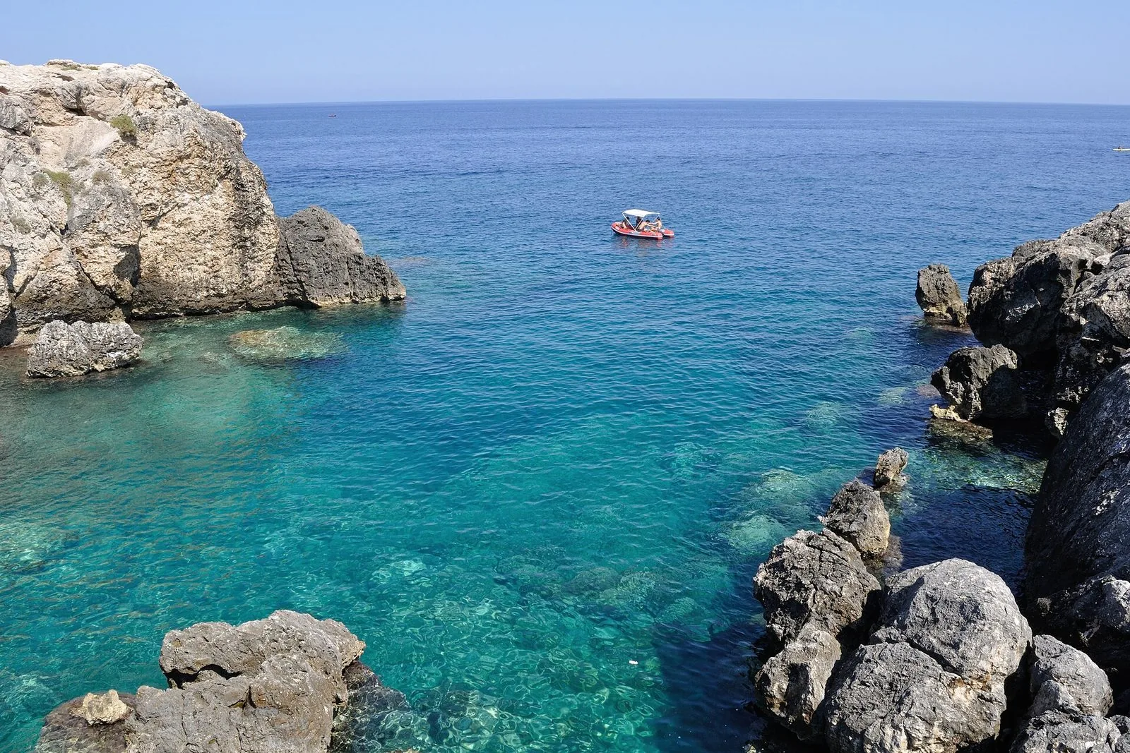 Una cala dell'isola di San Domino, alle Tremiti, con scogli chiari, acqua turchese trasparente e una piccola barca in mare aperto