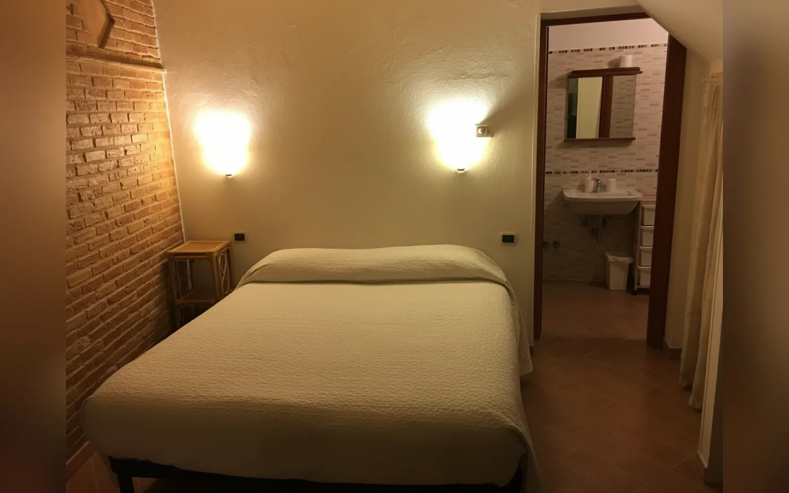 Il letto matrimoniale accanto alla parete in mattoni, con le applique accese