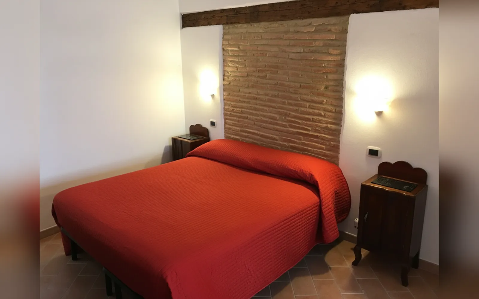 Il letto con il copriletto rosso e la parete in mattoni a vista