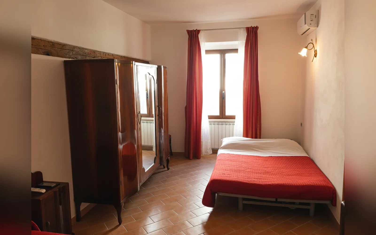 Il letto rosso, l’armadio in legno e la finestra con le tende rosse